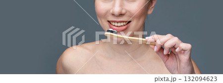Smiling caucasian female brushing teeth with eco-friendly bamboo toothbrush 132094623