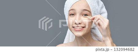 Young caucasian female applying eye patch with towel on head smiling skincare Young caucasian female applying eye patch with towel on head smiling skincare 132094682