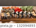A delicious, high-angle close-up shot of a large, colourful assortment of sushi rolls presented on a rustic wooden board, showcasing a variety of textures and ingredients 132094893