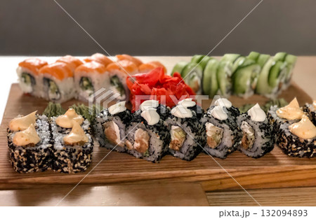 A delicious, high-angle close-up shot of a large, colourful assortment of sushi rolls presented on a rustic wooden board, showcasing a variety of textures and ingredients 132094893
