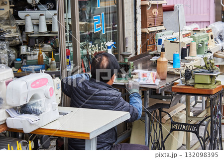 A man working with sewing machines and tools outside a shop in Busan, South Korea A man working with sewing machines and tools outside a shop in Busan, South Korea 132098395