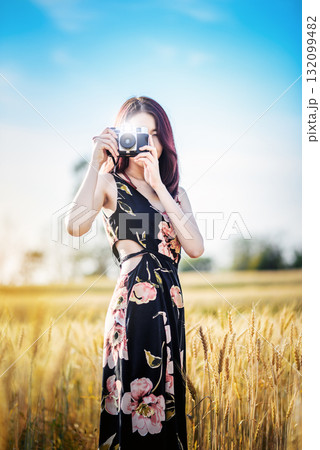 Charming asian woman Photographer holding camera on wheat summer fields in warm sunset Charming asian woman Photographer holding camera on wheat summer fields in warm sunset 132099482