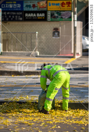 A worker in bright green uniform gathering fallen yellow leaves on a sidewalk in Seoul, South Korea A worker in bright green uniform gathering fallen yellow leaves on a sidewalk in Seoul, South Korea 132099638