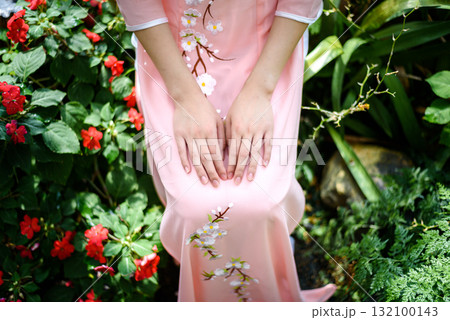 Portrait of Asian girls with Ao-Dai Vietnam traditional dress costume  sitting in flower garden 132100143