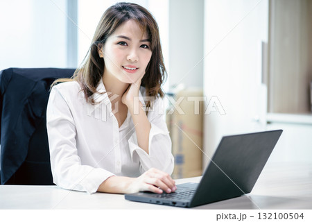Happy attractive asian business woman smiling working with laptop in modern office 132100504
