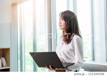 Happy attractive asian business woman smiling working with laptop in modern office 132100506