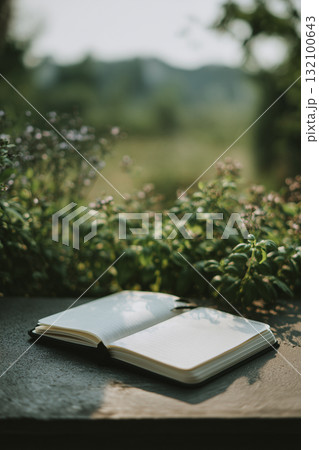 Open notebook on a table surrounded by nature in a peaceful outdoor setting 132100643