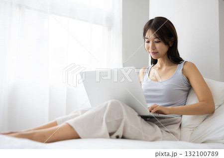 ベッドの上でノートパソコンを操作する若い女性 ベッドの上でノートパソコンを操作する若い女性 132100789