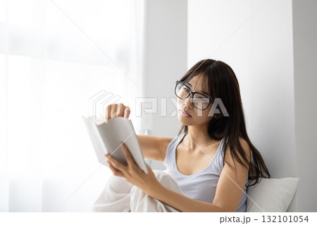 ベッドで読書をするメガネをかけた若い女性 132101054