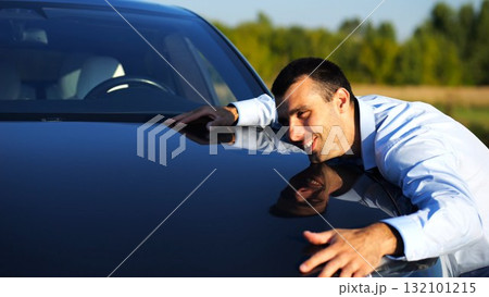 Successful smiling manager bought new electrical vehicle and hugging hood of auto. Happy young businessman in shirt enjoying modern electric automobile. Concept of buy or rent car. Slow motion 132101215