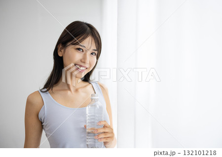 窓辺でペットボトルの水を持ち微笑む若い女性 窓辺でペットボトルの水を持ち微笑む若い女性 132101218