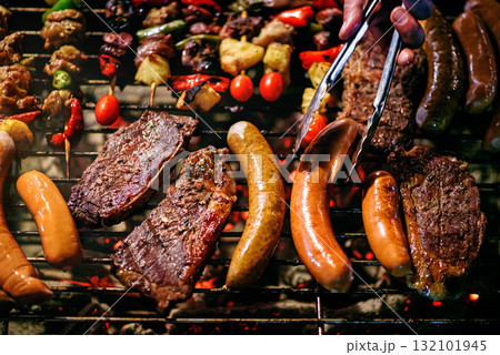 chef grilling steaks with grilled sausages and  skewers barbecue 132101945