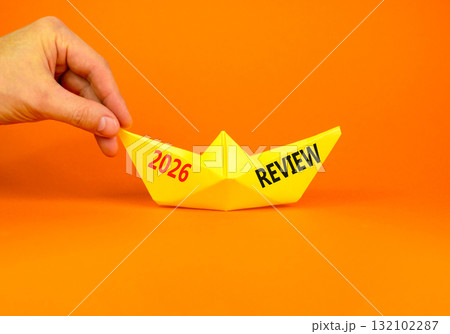 2026 Review symbol. Concept words 2026 Review on beautiful yellow paper boat. Beautiful orange paper background. Businessman's hand. Business and 2026 review concept. Copy space. 2026 Review symbol. Concept words 2026 Review on beautiful yellow paper boat. Beautiful orange paper background. Businessman's hand. Business and 2026 review concept. Copy space. 132102287