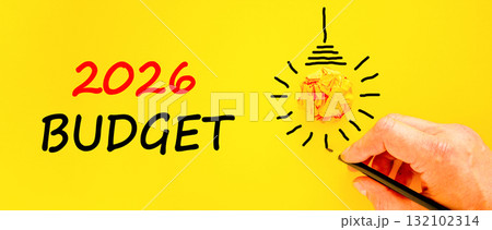 2026 Budget symbol. Concept words 2026 Budget on beautiful yellow paper. Beautiful orange paper background. Light bulb icon. Businessman's hand with pen. Business and 2026 budget concept. Copy space. 132102314