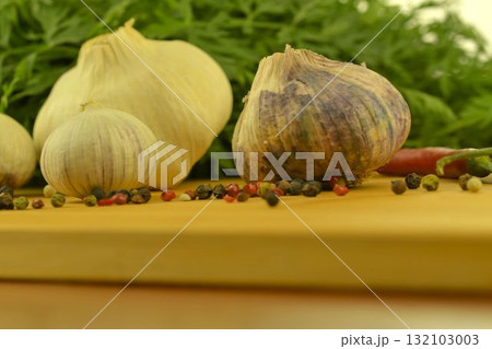 A bulb of garlic, red chili peppers, four-color pepper, and carrot tops on a wooden cutting board. The concept of cooking and vegetables in the home. Macro image, close-up. Garlic - Allium sativum is 132103003