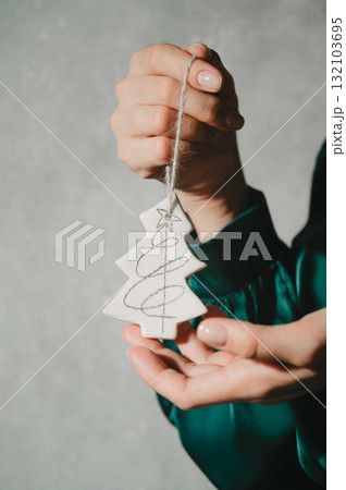 Closeup of woman's hands holding handmade ceramic porcelain Christams ornaments of a fir tree Closeup of woman's hands holding handmade ceramic porcelain Christams ornaments of a fir tree 132103695
