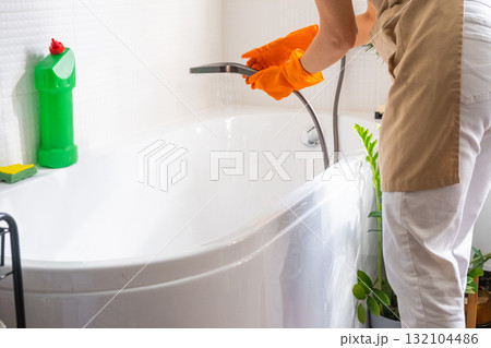 Woman in rubber gloves and apron manually washes bathtub is in bathroom of house with sponge cleaner and cleaning agent in a bottle. Restoring order, cleanliness and hygiene in home, cleaning servise Woman in rubber gloves and apron manually washes bathtub is in bathroom of house with sponge cleaner and cleaning agent in a bottle. Restoring order, cleanliness and hygiene in home, cleaning servise 132104486