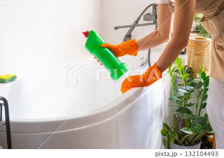 Woman in rubber gloves and apron manually washes bathtub is in bathroom of house with sponge cleaner and cleaning agent in a bottle. Restoring order, cleanliness and hygiene in home, cleaning servise Woman in rubber gloves and apron manually washes bathtub is in bathroom of house with sponge cleaner and cleaning agent in a bottle. Restoring order, cleanliness and hygiene in home, cleaning servise 132104493
