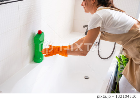 Woman in rubber gloves and apron manually washes bathtub is in bathroom of house with sponge cleaner and cleaning agent in a bottle. Restoring order, cleanliness and hygiene in home, cleaning servise Woman in rubber gloves and apron manually washes bathtub is in bathroom of house with sponge cleaner and cleaning agent in a bottle. Restoring order, cleanliness and hygiene in home, cleaning servise 132104510