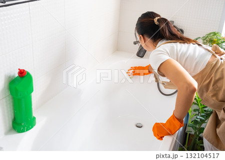 Woman in rubber gloves and apron manually washes bathtub is in bathroom of house with sponge cleaner and cleaning agent in a bottle. Restoring order, cleanliness and hygiene in home, cleaning servise Woman in rubber gloves and apron manually washes bathtub is in bathroom of house with sponge cleaner and cleaning agent in a bottle. Restoring order, cleanliness and hygiene in home, cleaning servise 132104517