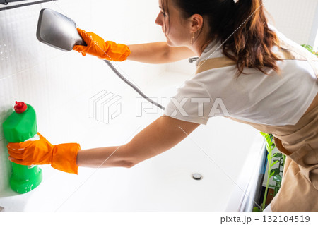 Woman in rubber gloves and apron manually washes bathtub is in bathroom of house with sponge cleaner and cleaning agent in a bottle. Restoring order, cleanliness and hygiene in home, cleaning servise Woman in rubber gloves and apron manually washes bathtub is in bathroom of house with sponge cleaner and cleaning agent in a bottle. Restoring order, cleanliness and hygiene in home, cleaning servise 132104519