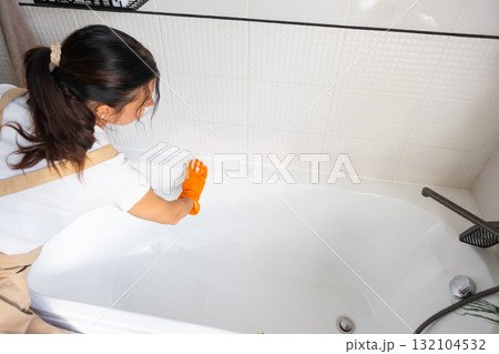 Woman in rubber gloves and apron manually washes bathtub is in bathroom of house with sponge cleaner and cleaning agent in a bottle. Restoring order, cleanliness and hygiene in home, cleaning servise Woman in rubber gloves and apron manually washes bathtub is in bathroom of house with sponge cleaner and cleaning agent in a bottle. Restoring order, cleanliness and hygiene in home, cleaning servise 132104532