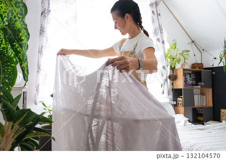 A housewife woman in an apron irons linen curtains in a room on an ironing board A housewife woman in an apron irons linen curtains in a room on an ironing board 132104570