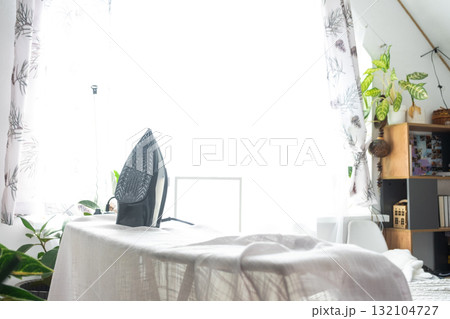 The iron is on the ironing board with a plain cloth in the room in close-up. 132104727