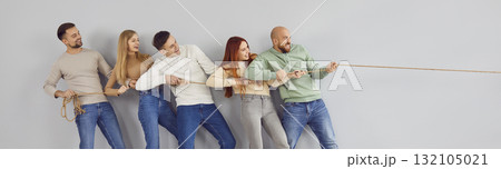 Group of happy smiling friends playing tug of war on grey color banner background Group of happy smiling friends playing tug of war on grey color banner background 132105021