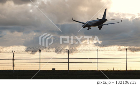 Passenger plane landing at airport behind barbed wire fence at sunset Passenger plane landing at airport behind barbed wire fence at sunset 132106215