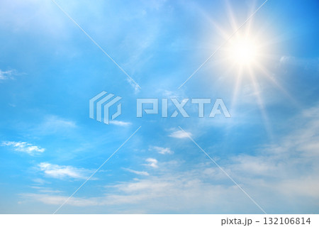 Bright blue sky with shining sun in upper corner and scattered white clouds illuminated by sun rays creating glowing daytime atmosphere with copy space 132106814