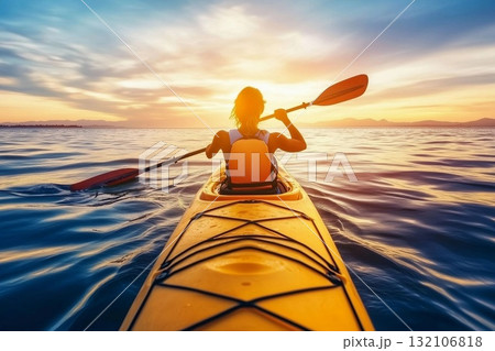Sunset kayaking on tranquil waters with a person paddling in a bright yellow kayak near a shoreline at dusk 132106818