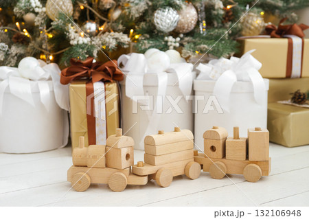 Wooden toy train with festive gift boxes under decorated Christmas tree in holiday interior 132106948