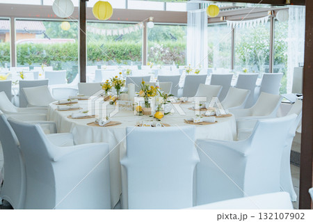 Stylish round table decorated with white linens and yellow floral centerpieces set for a formal event. Elegant chairs and bright surroundings enhance the sophisticated atmosphere 132107902