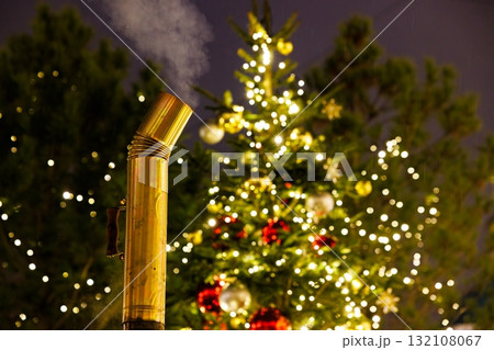 Brass pipe emitting steam near a beautifully decorated Christmas tree at night 132108067