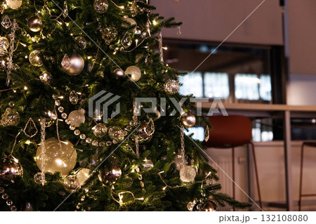 Sparkling Christmas tree adorned with silver ornaments and glowing lights in a cozy indoor setting Sparkling Christmas tree adorned with silver ornaments and glowing lights in a cozy indoor setting 132108080