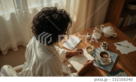 Dark-Skined Woman Writing in a Notebook by the Window 132108340