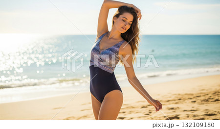 A stunning outdoor, mid-shot photograph of an attractive young woman standing on a sandy beach at sunset or sunrise. 132109180