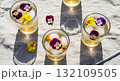 Overhead View Of Cocktails With Edible Flowers And Ice Cubes On A Striped Surface Illuminated By Sunlight 132109505