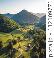 Aerial View Of A Lush Green Valley At Sunset With Rolling Hills Houses And Forest Paths Illuminated By Golden Light 132109771