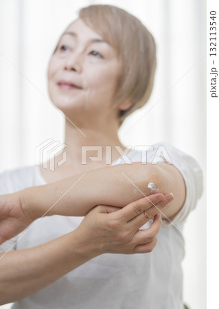 肘のカサつきにクリームを塗るシニア女性 132113540