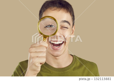 Boy looking through a magnifying glass isolated on a studio beige background. Boy looking through a magnifying glass isolated on a studio beige background. 132113881