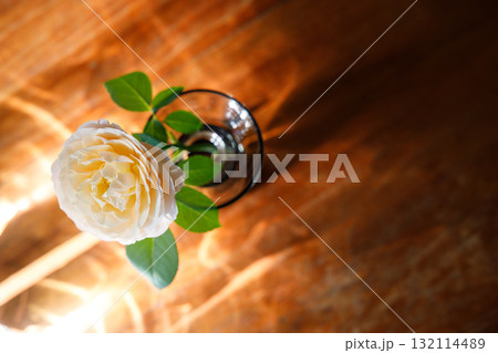 Yellow beautiful blooming rose in glass vase under window light on wooden table. Yellow beautiful blooming rose in glass vase under window light on wooden table. 132114489
