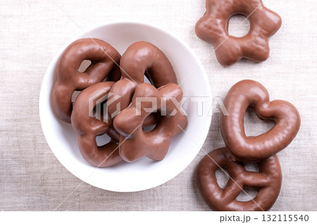 Chocolate dipped gingerbread, in a white bowl, on linen. Heart and star shaped traditional German Lebkuchen, fully coated with milk chocolate. Spicy gingerbread, fluffy and soft like a cake. Photo Chocolate dipped gingerbread, in a white bowl, on linen. Heart and star shaped traditional German Lebkuchen, fully coated with milk chocolate. Spicy gingerbread, fluffy and soft like a cake. Photo 132115540