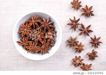 Star anise seeds, fruits and seeds, in a white bowl on linen. Star shaped fruits of Illicium verum, also known as badian, and as star aniseed, a spice, that closely resembles anise in flavor. Photo 132115541