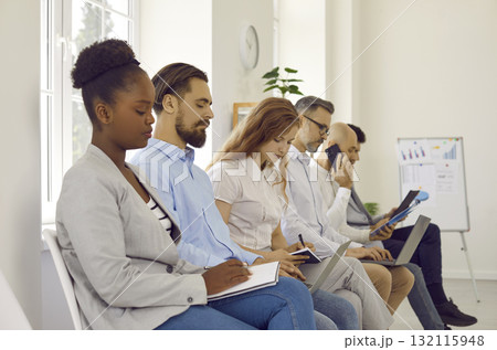 Multiracial business people making notes on corporative education sitting in row in office. Multiracial business people making notes on corporative education sitting in row in office. 132115948
