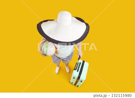 Funny high angle shot of woman with big sun hat, beach ball and suitcase on summer holiday 132115980