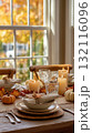 Elegant autumn dining table decorated with candles, pumpkins, and fall leaves near a bright window 132116096