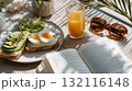 Healthy breakfast with avocado toast, boiled egg, and orange juice beside an open book and sunglasses 132116148