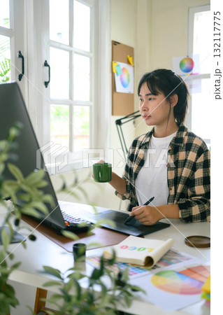 Graphic designer creating logo on digital tablet in bright modern workspace with computer and color palette Graphic designer creating logo on digital tablet in bright modern workspace with computer and color palette 132117775